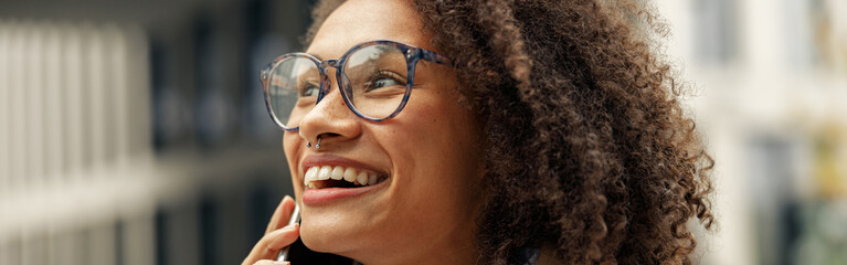Close up of afro american woman wearing glasses talking phone with friends during city walking