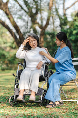 Young asian care helper with asia elderly woman on wheelchair relax together park outdoors to help and encourage and rest your mind with green nature. Use a stethoscope to listen to your heartbeat.