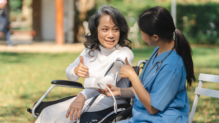 Young asian care helper with asia elderly woman on wheelchair relax together park outdoors to help and encourage and rest your mind with green nature. measure blood pressure