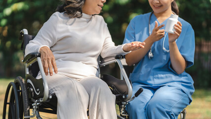 Young asian care helper with asia elderly woman on wheelchair relax together park outdoors to help...