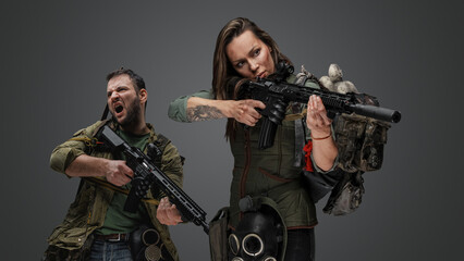 Studio shot of woman aiming rifle and screaming guy in setting of post apocalypse. - obrazy, fototapety, plakaty