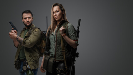 Studio shot of post apocalyptic couple survivors with guns against gray background.