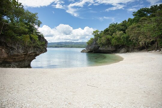 Idyllic, secluded beach of Siquijor in the Philippines with white sand and crystal clear water in a small bay with trees and cliffs.
