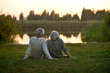 Elderly couple sits on the shore of a lake. Rear view.