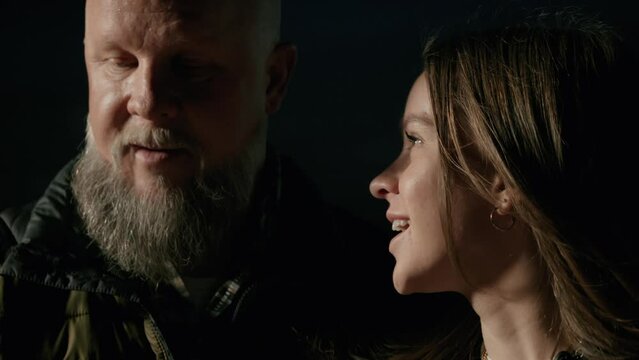 A young female teenager and father enjoy a laughing conversation while gathered around a firepit in the cold night air.  Shot in glorious 4k.