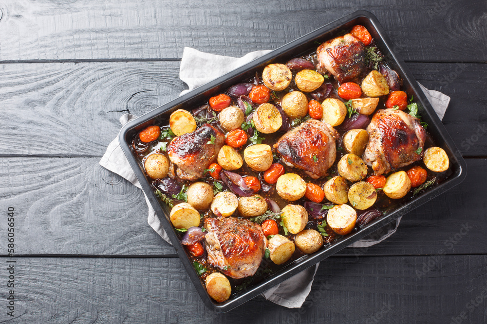 Canvas Prints chicken thighs baked with potatoes, garlic, onions and tomatoes close-up on a black baking sheet on 