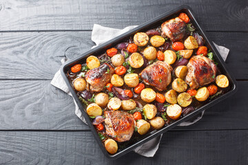 Chicken thighs baked with potatoes, garlic, onions and tomatoes close-up on a black baking sheet on...