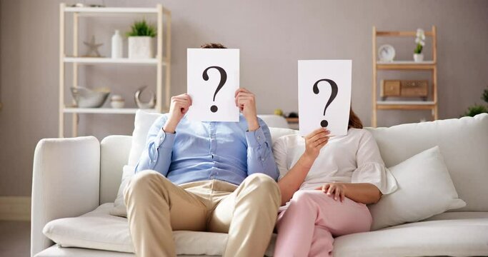 Couple Sitting On Sofa Holding Question Mark Sign In Front