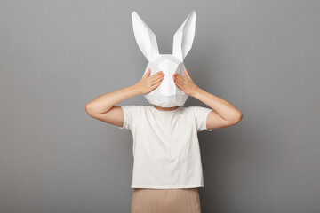 Portrait of scared anonymous woman wearing white t shirt and paper rabbit mask standing covering...