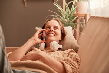 Portrait of smiling attractive beautiful girl talking mobile phone, spending time at home, relaxing on sofa, talking with friend or boyfriend, expressing positive emotions.