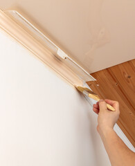 A worker paints moldings on the ceiling with a brush. Home renovation.