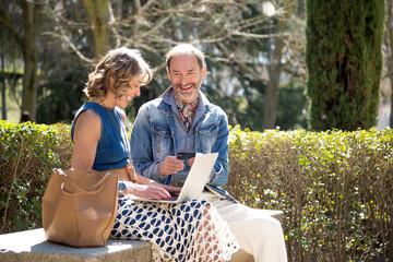 a middle-aged couple with their credit card doing online shopping with their computer sitting in the park