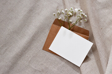 Empty paper card with mockup copy space, envelope, flowers on neutral beige linen background,...