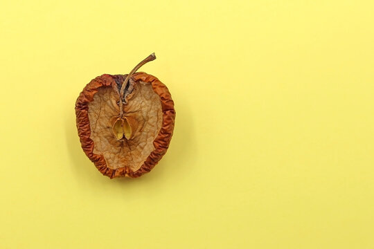 A ripe and spoiled apple cut in half on a yellow background
