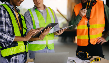  colleagues discussing data working and tablet, laptop with on on architectural project at construction site at desk in office.