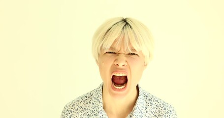Emotional irritated blonde woman squints and open mouth screaming loud. Expressive female person shows aggression standing on beige background slow motion
