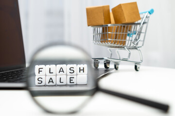 Flash sale word on cubes through a magnifying glass and with a toy shopping cart with boxes on the...