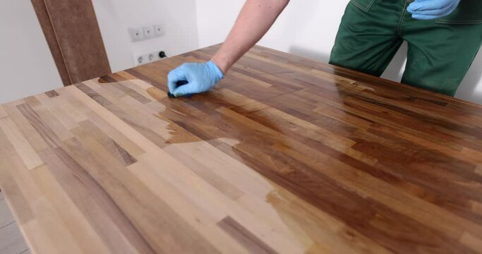 Carpenter processes wooden flooring surface with varnish