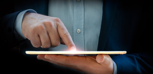 Businessman in a blue suit holding a tablet with one hand and touching the screen with the other hand - Flare on finger - Business, strategy, marketing and finance background