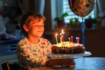Adorable happy blond little kid boy celebrating his birthday. Child blowing seven candles on...