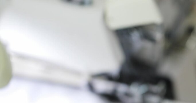 the hands of a seamstress sewing a white fabric with an overlock sewing machine on the production of dresses. close-up. cuts white thread with scissors.
