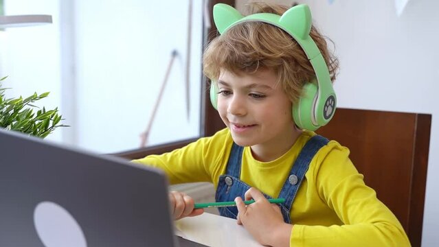 Cute smart caucasian primary School Child with headphones educate online laptop. Tutor teaching digital class, web lesson on computer at home. Virtual education course. Schoolboy girl studying doing
