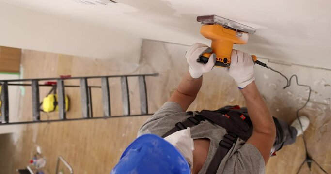 Builder with respirator uses electric polisher to grind wall
