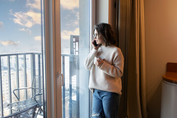woman speaking on phone near window at home 