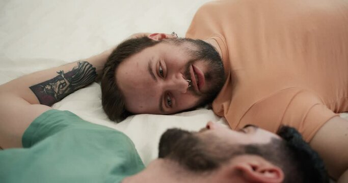Portrait of attractive bearded gay men couples laying on bed together, talking