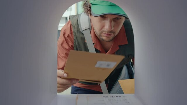 Postman putting letters and parcel into mailbox and closing it while working in postal service. POV shot from inside of the mailbox