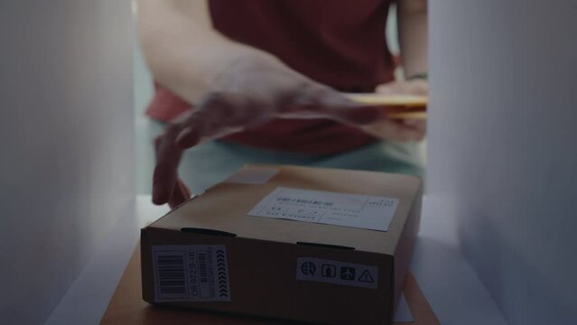 Hands of unrecognizable person taking letters and parcel box out of the personal mailbox. POV shot from inside of the mailbox
