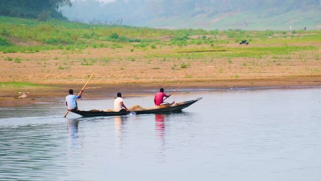 Three Asian gypsy fishermen rowing a wooden boat on a river in Bangladesh.