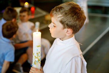 Little kid boy receiving his first holy communion. Happy child holding Christening candle....