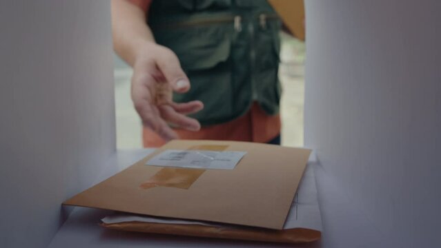 Unrecognizable postman putting letters and parcel box into mailbox and then closing it. POV shot from inside of the mailbox