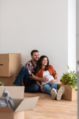 Beautiful young couple expecting a baby just moved into an empty apartment, sitting among cardboard boxes making plans for the future. New beginnings