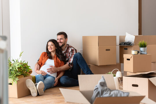 Beautiful young couple expecting a baby just moved into an empty apartment, sitting among cardboard boxes making plans for the future. New beginnings