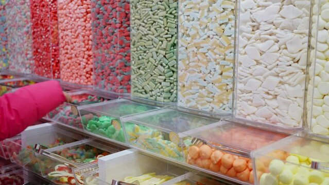 Little girl, buyer selects the beans candy in the store, slow motion