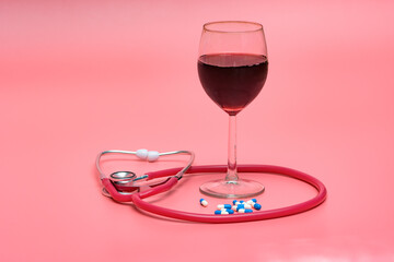 Kieliszek z czerwonym winem i stetoskopem medycznym na różowym tle