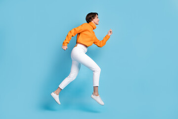 Fototapeta na wymiar Full size photo of pretty young girl profile view running hurry speed fast dressed stylish orange look isolated on blue color background