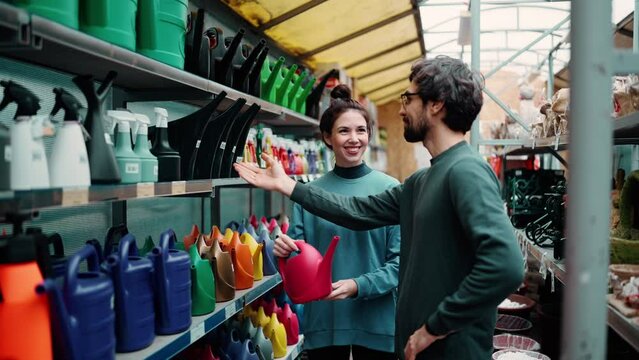 Portrait of positive young couple at the garden store, choosing watering can