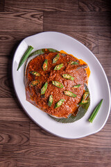 grilled bbq fresh whole seafood stingray fish with spicy samba chilli sauce and lady finger vegetables on banana leaf plate wood table asian halal food menu