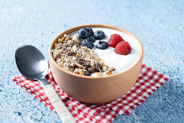 Yogurt with berries and muesli for breakfast in bowl on blue background