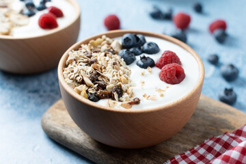 Yogurt with berries and muesli for breakfast in bowl on blue background