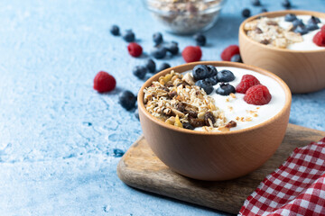 Yogurt with berries and muesli for breakfast in bowl on blue background. Copy space
