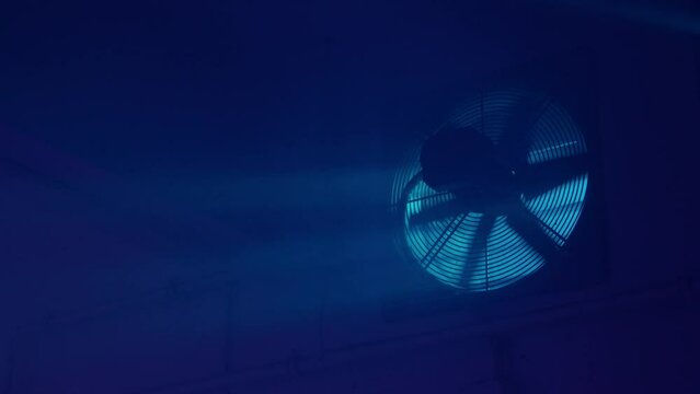 Interior night shot of an empty basement. Blue light, dirty window and fan. 