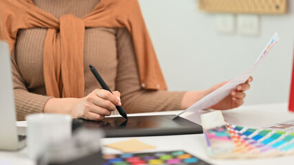 Cropped shot, selective focus on hand. Creative woman using graphic tablet and working with color swatch samples at workplace