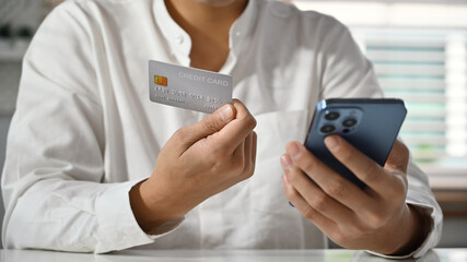Cropped image of man holding using mobile phone and credit cad for online banking transaction, ordering in internet