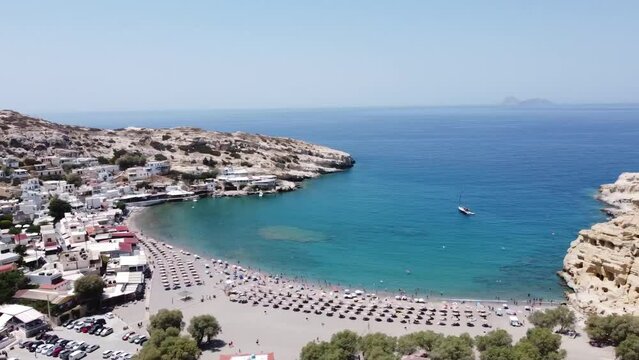 Aerial drone view of famous Matala beach with caves, known for hippies in the 70's. View of the beach from rock caves, once a roman cemetery, in famous greek beach Matala, Crete, Greece.