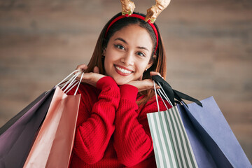 Portrait, christmas headband and female with shopping bags for a festive or holiday celebration. Happy, smile and face of a woman model with gifts or presents with xmas reindeer ears for an event. © Talia Mdlungu/peopleimages.com