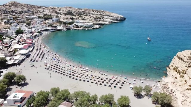 Aerial drone view of famous Matala beach with caves, known for hippies in the 70's. View of the beach from rock caves, once a roman cemetery, in famous greek beach Matala, Crete, Greece.